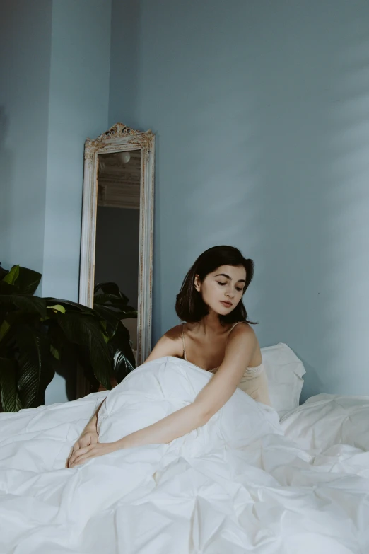 a woman sitting on top of a bed covered in white sheets, inspired by Elsa Bleda, unsplash contest winner, classical realism, pale blue skin, portrait of alexandra daddario, photoshoot for skincare brand, over-shoulder shot