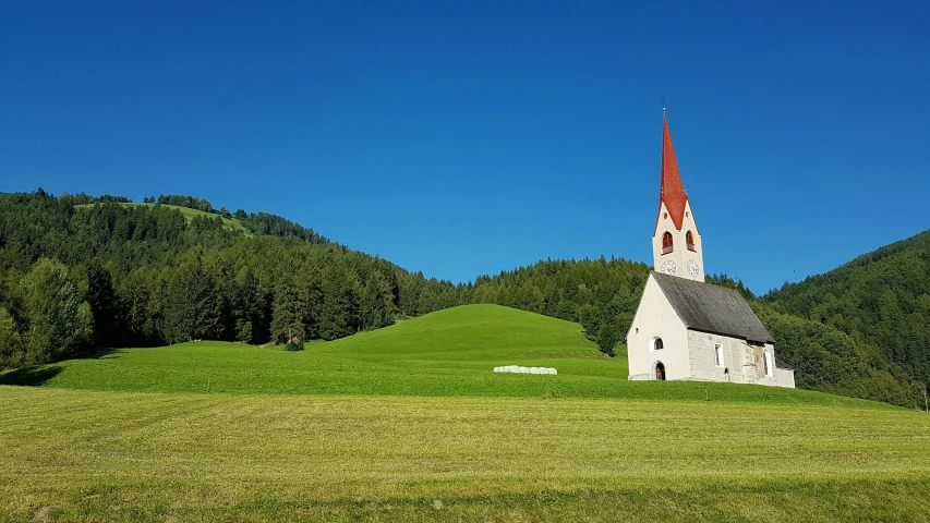 a church sitting on top of a lush green hillside, an album cover, by Werner Andermatt, pexels contest winner, blue sky and green grassland, red peaks in the background, profile picture 1024px, pastures