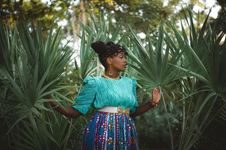 a woman standing in front of a palm tree, by Lily Delissa Joseph, pexels contest winner, afrofuturism, teal skirt, wearing an ornate outfit, young southern woman, sza