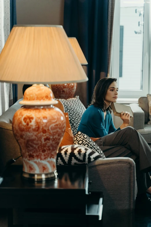 a woman sitting on a couch in a living room, by Adam Marczyński, pexels contest winner, orange lamp, hotel room, still image from tv series, thoughtful )