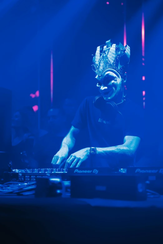 a man that is standing in front of a dj, wearing a bejeweled mask, sitting down, headroom, ray swanland