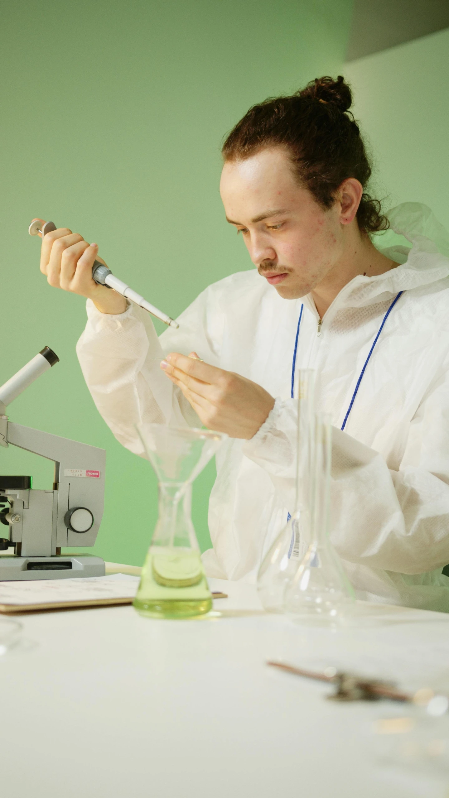 a woman sitting at a table in front of a microscope, an album cover, pexels, one single man in a hazmat suit, plants in scientific glassware, thin young male alchemist, concentrated
