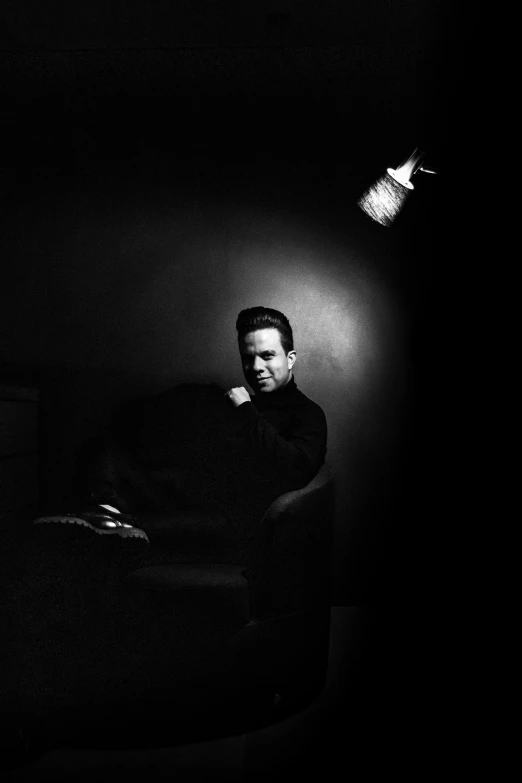 a man sitting on a couch in a dark room, inspired by Yousuf Karsh, bauhaus, tyler durden, black main color, square, ewan mcgregor