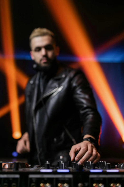 a man that is standing in front of a mixer, an album cover, by Robbie Trevino, trending on pexels, wearing a black leather jacket, light beard, in a nightclub, blonde man