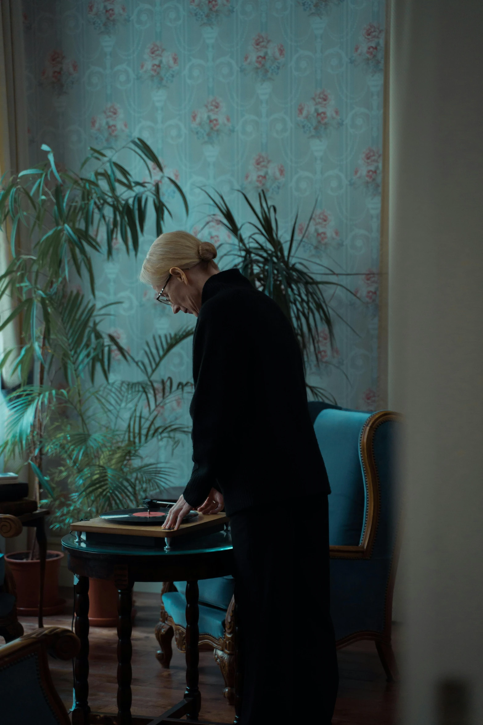 a woman standing in a living room next to a table, an album cover, inspired by Elsa Bleda, unsplash, white haired lady, scratches and burns on film, ignant, ! movie scene