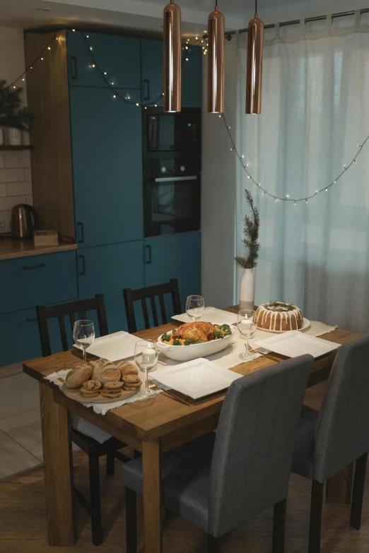a wooden table topped with plates of food, by Adam Marczyński, pexels contest winner, city apartment cozy calm, christmas night, kitchen, blue