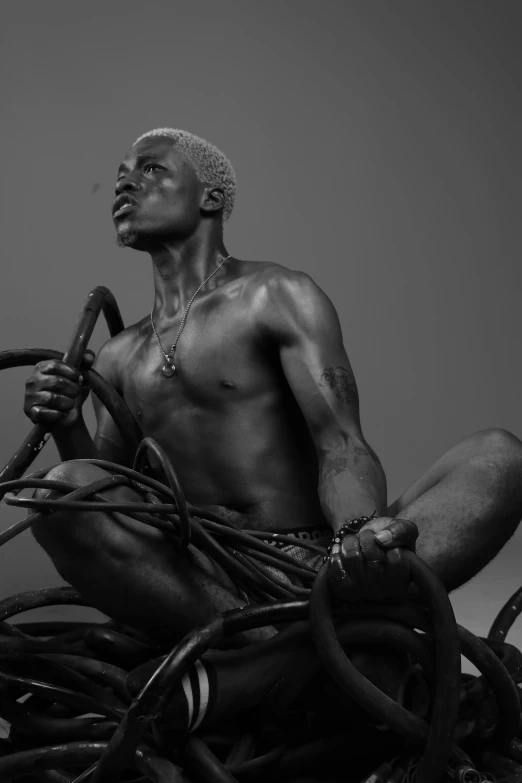 a man sitting on top of a pile of wires, an album cover, inspired by Candido Bido, pexels contest winner, afrofuturism, beautiful male drow, body building blacksmith, showstudio, silver haired