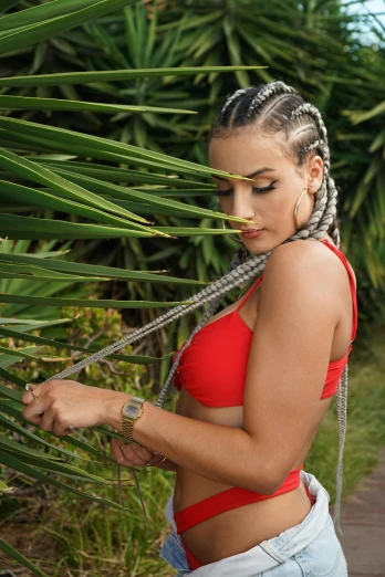 a woman in a red top standing next to a palm tree, an album cover, inspired by Lili Árkayné Sztehló, trending on pexels, rasquache, white braids, sport bra, portrait of demi rose, profile image