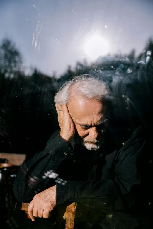 a man sitting on top of a wooden chair, an album cover, inspired by Lajos Vajda, unsplash, ray of light through white hair, looking exhausted, nature outside, a man wearing a black jacket