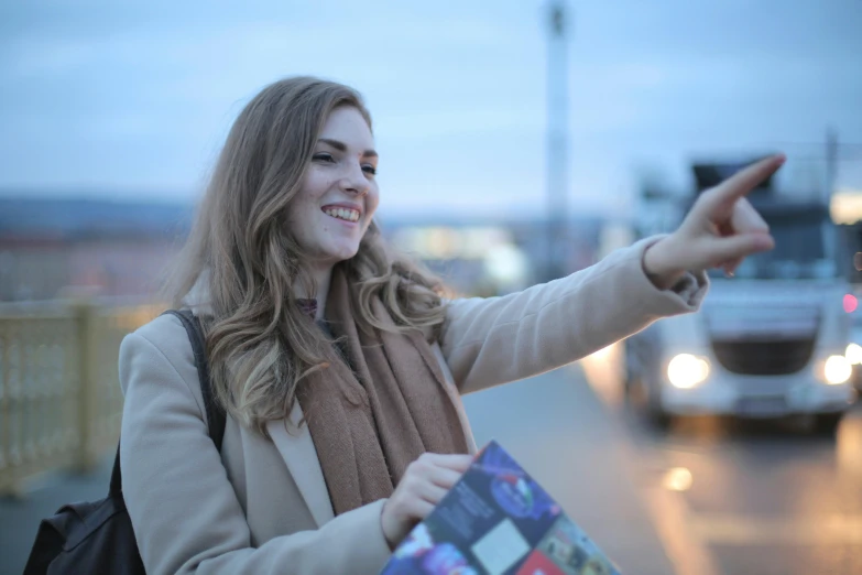 a woman pointing at a bus on a city street, by Niko Henrichon, pexels contest winner, happening, square, avatar image, holding a nintendo switch, warm light