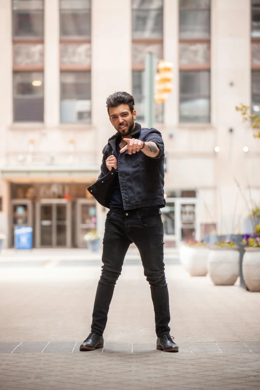 a man standing in the middle of a street pointing at something, by Adam Dario Keel, wearing a jeans jackets, promo image, mogul khan, man standing in defensive pose