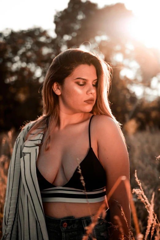 a woman standing in a field of tall grass, inspired by Elsa Bleda, unsplash, buxom chested, alluring plus sized model, ((sunset)), trending photo