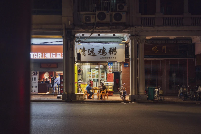 a man sitting on a chair in front of a store, by Patrick Ching, pexels contest winner, nightcap, chinese building, family dinner, storefront
