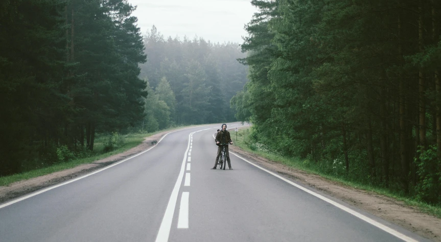 a man riding a bike down the middle of a road, by Jaakko Mattila, near forest, couple, standing in road, ignant