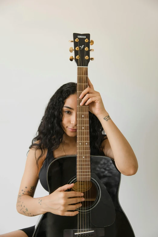 a woman in a black dress holding a guitar, riyahd cassiem, on clear background, light skin, an olive skinned