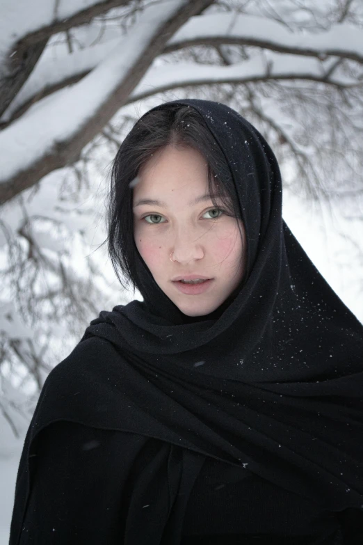 a woman wearing a black shawl in the snow, an album cover, inspired by Steve McCurry, pexels contest winner, hyperrealism, a young woman as genghis khan, looking to camera, islamic, russian girlfriend
