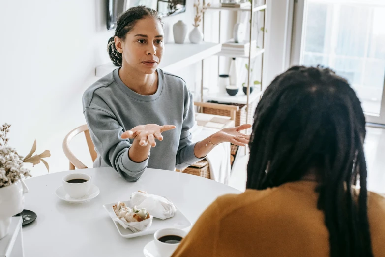 two women sitting at a table having a conversation, pexels contest winner, 💣 💥💣 💥, reaching out to each other, foreground focus, brown