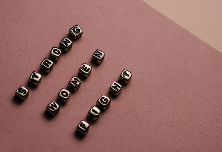 a bunch of metal letters sitting on top of a pink surface, by Emma Andijewska, trending on pexels, letterism, dices, strong woman, brown, broken lights