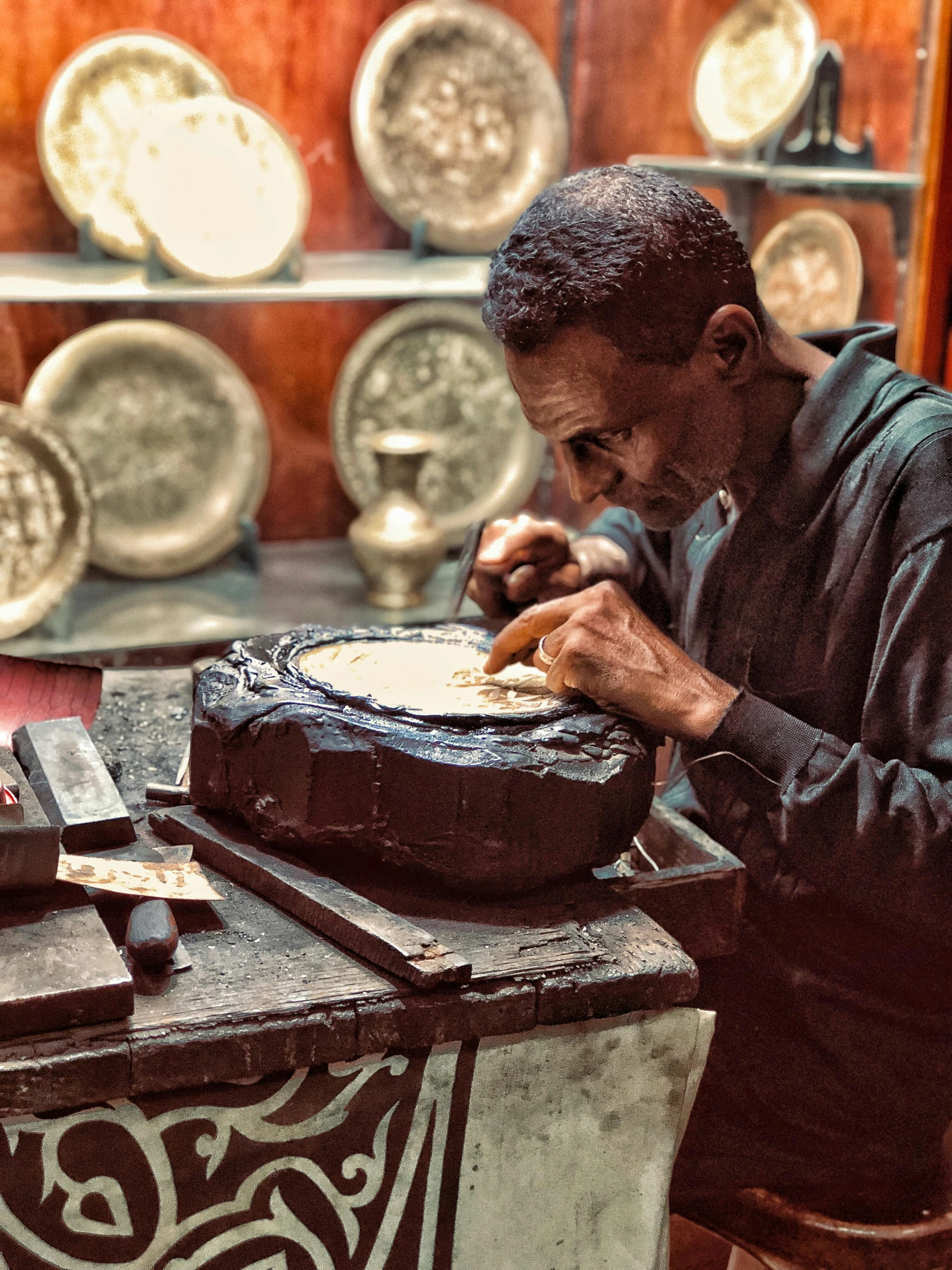 a man sitting at a table working on a piece of pottery, an album cover, inspired by Afewerk Tekle, pexels contest winner, made of polished broze, damascus, 278122496, maintenance photo