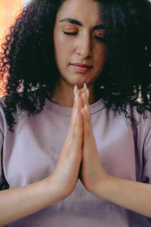 a woman with her hands folded in prayer, an album cover, pexels, wearing purple undershirt, avatar image, curls, religion