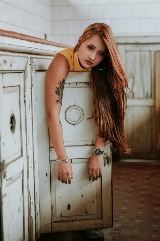 a woman leaning on a cabinet in a kitchen, inspired by Elsa Bleda, trending on pexels, renaissance, rusty colored long hair, tattoos, teenager girl, attractive photo