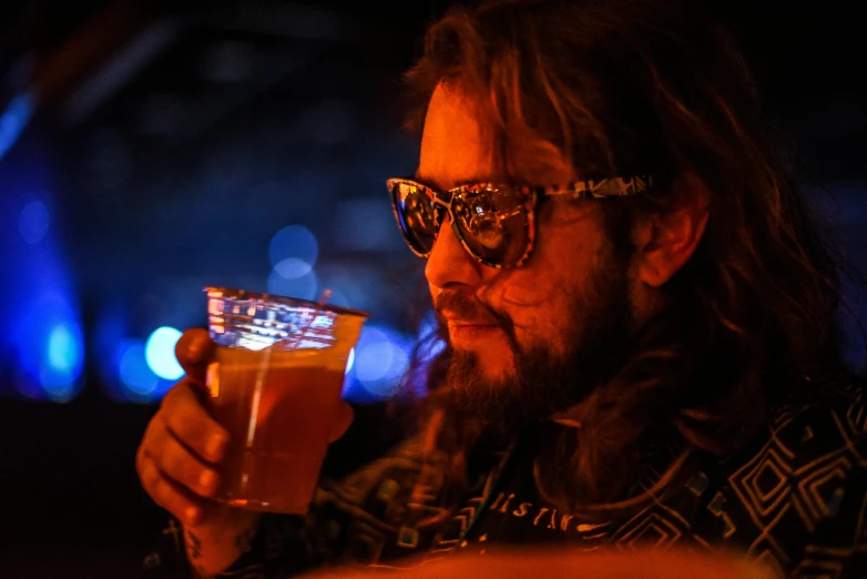 a man with long hair holding a glass of beer, at a rave, profile image, bearded, amber glasses