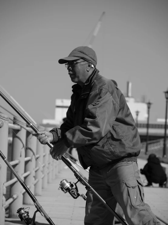 a black and white photo of a man holding a fishing rod, a black and white photo, by Sam Charles, on a bridge, 2006 photograph, wearing sunglasses and a cap, working hard