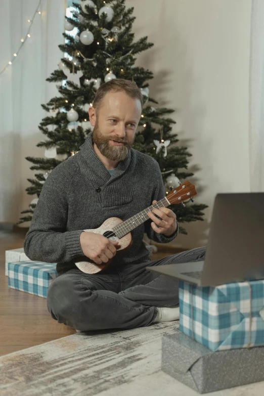 a man sitting on the floor playing a guitar, inspired by Ernest William Christmas, reddit, using a macbook, wearing festive clothing, video still, ukulele