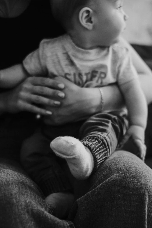 a black and white photo of a woman holding a baby, a black and white photo, by Felix-Kelly, pexels, focus on his foot, sitting with wrists together, closeup of arms, childish look