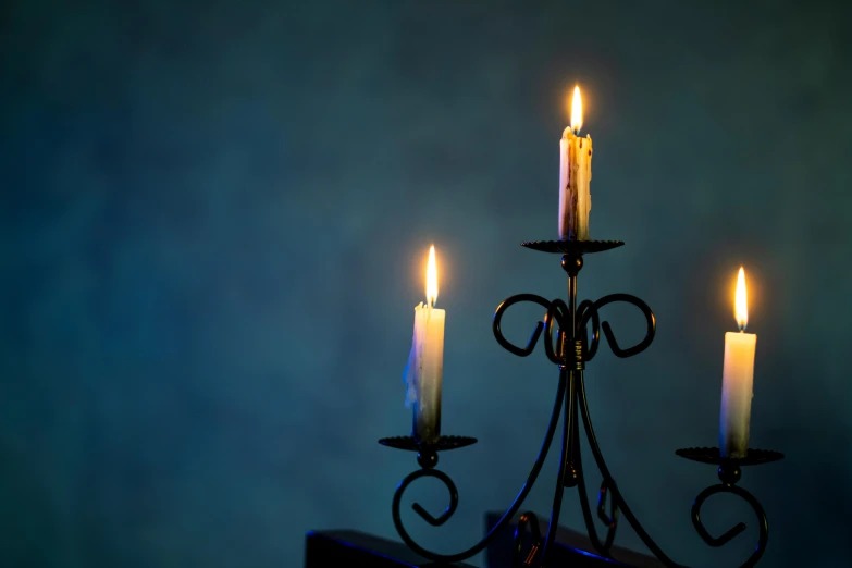 a group of three lit candles sitting on top of a table, an album cover, unsplash, romanticism, wrought iron, blue and green light, standing in a dimly lit room, background image