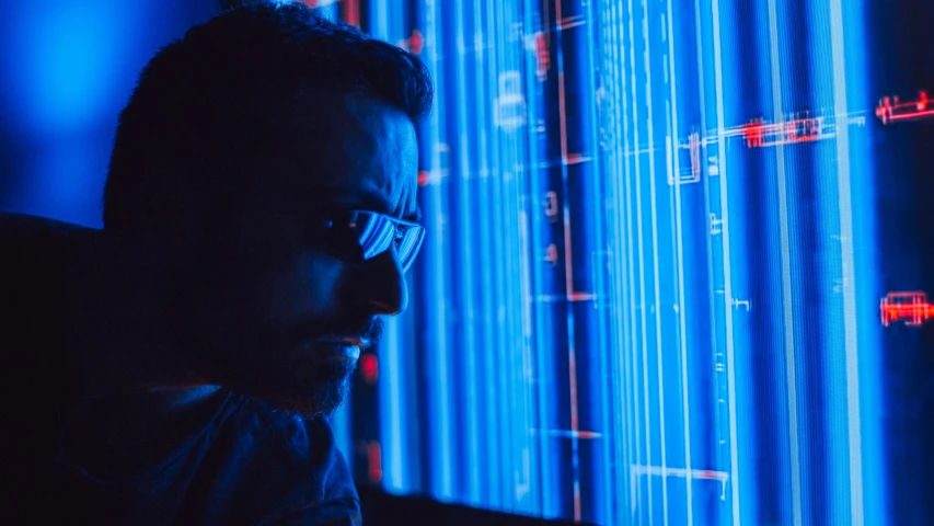 a man sitting in front of a computer screen, cyberpunk art, by Adam Marczyński, pexels, holography, background is data server room, blue color grading, man with glasses, close up to the screen