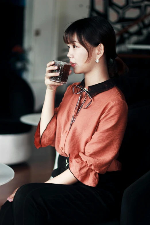 a woman sitting on a couch drinking from a glass, pexels, shin hanga, collared shirt, black and terracotta, 奈良美智, tiffany style