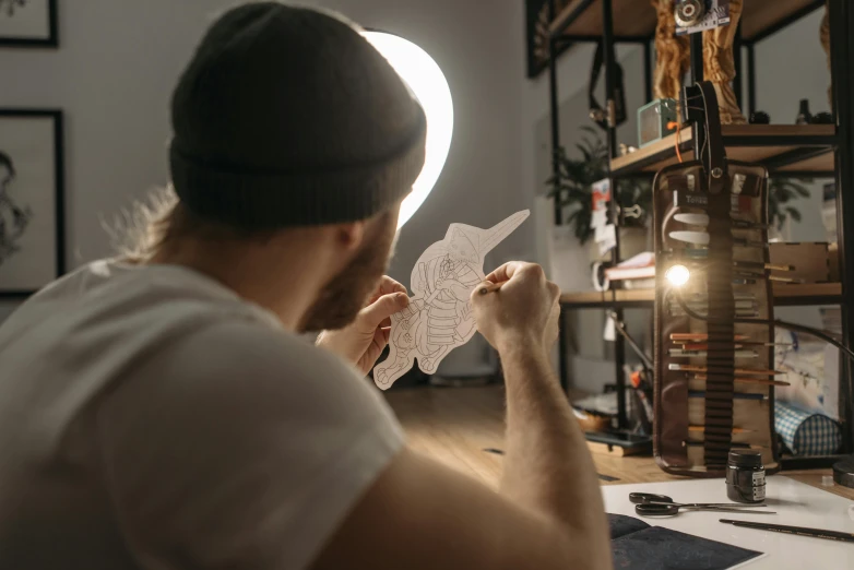 a man sitting at a desk holding a piece of paper, pexels contest winner, arbeitsrat für kunst, dinosaur wood carving, lights on, in a studio, guitar shape build