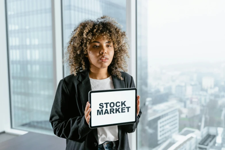 a woman holding a sign that says stock market, a stock photo, by Andries Stock, pexels contest winner, renaissance, mixed race, square, brown, 8k hq