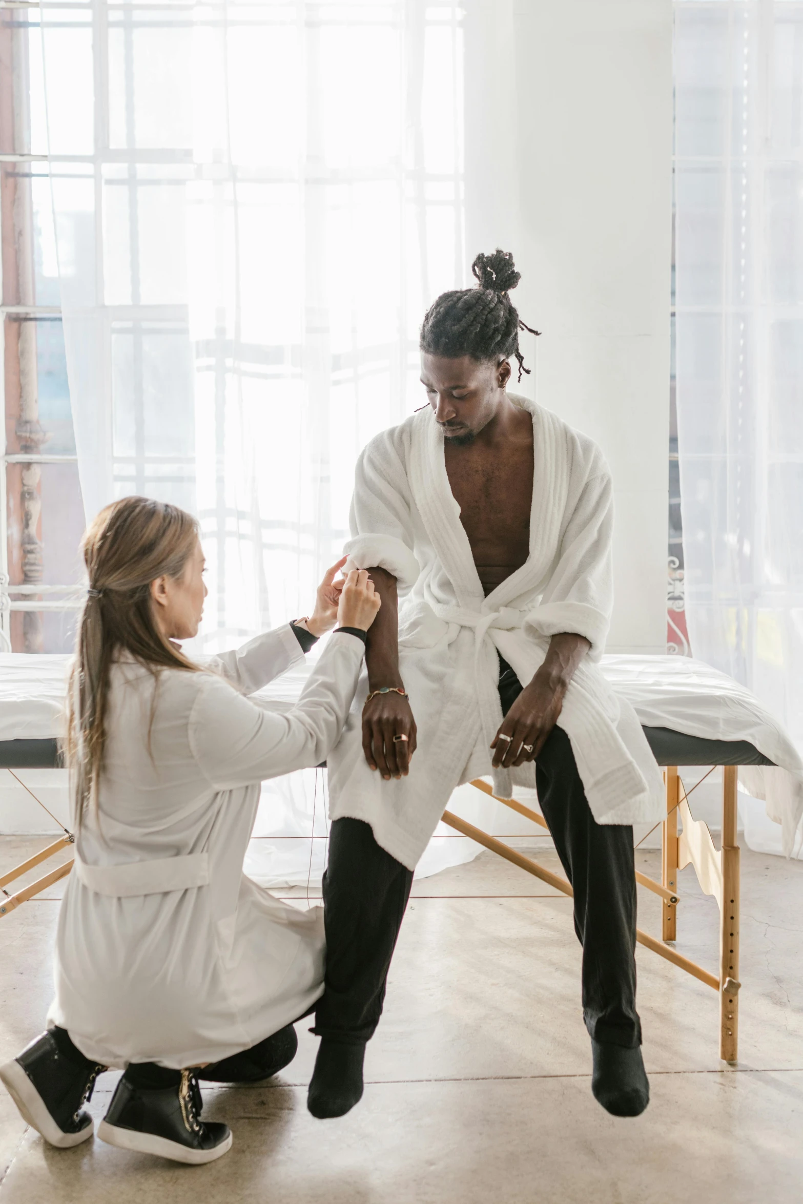 a man sitting on top of a bed next to a woman, pexels contest winner, renaissance, wearing a white lab coat, serving body, black man, acupuncture treatment