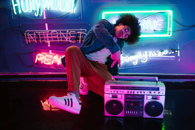 a man sitting on top of a boombox in front of neon signs, trending on pexels, wearing adidas clothing, jeffrey wright, dance party, finn wolfhard