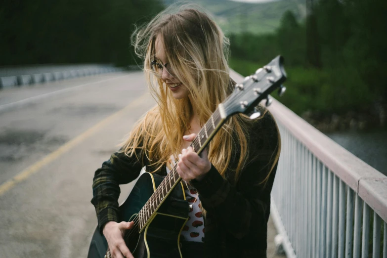 a woman holding a guitar on a bridge, pexels contest winner, girl wearing round glasses, flowing blonde hair, overcast mood, ( ( emma lindstrom ) )