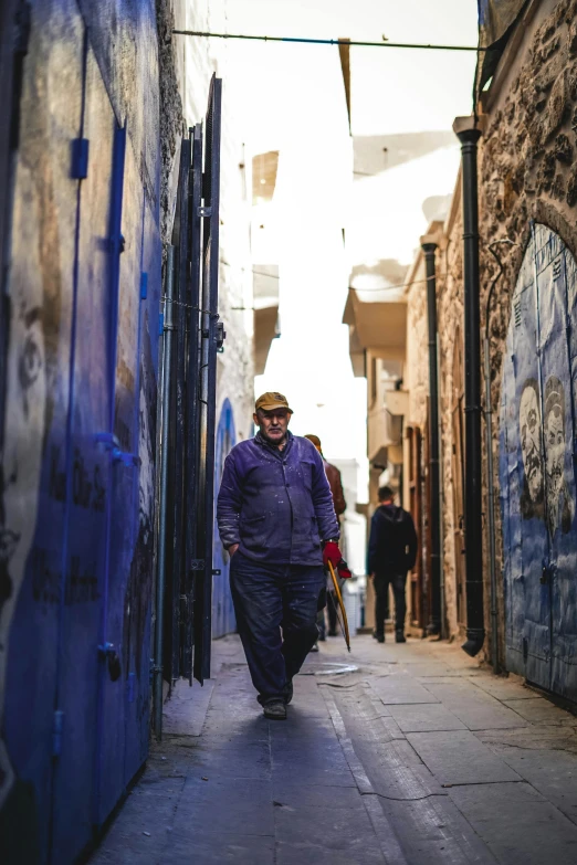 a man walking down a narrow alley way, inspired by Steve McCurry, graffiti, dressed in blue, patagonian, an oldman, an arab standing watching over