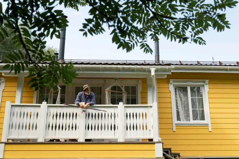 a man sitting on the balcony of a yellow house, inspired by Carl Larsson, unsplash, “ iron bark, photographed for reuters, sunday afternoon, shishkin