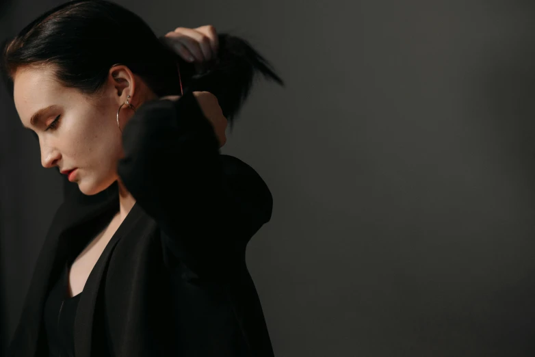 a woman combing her hair against a black background, trending on pexels, minimalism, black coat, black hair ribbons, cinematic outfit photo, side profile artwork