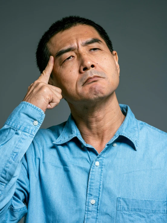 a man in a blue shirt holding his hand to his forehead, inspired by Zhang Xiaogang, thoughtful pose, ernie chan, tinnitus, asian descent