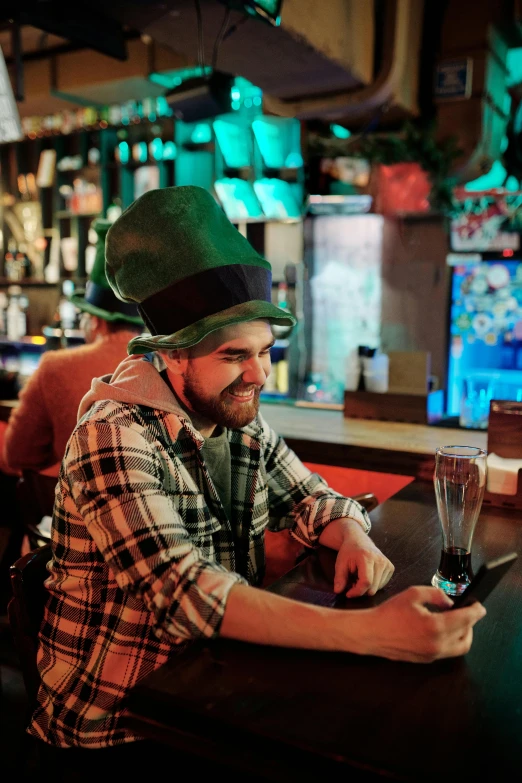 a man sitting at a bar using a cell phone, wearing green tophat, 🚀🌈🤩, irish genes, app