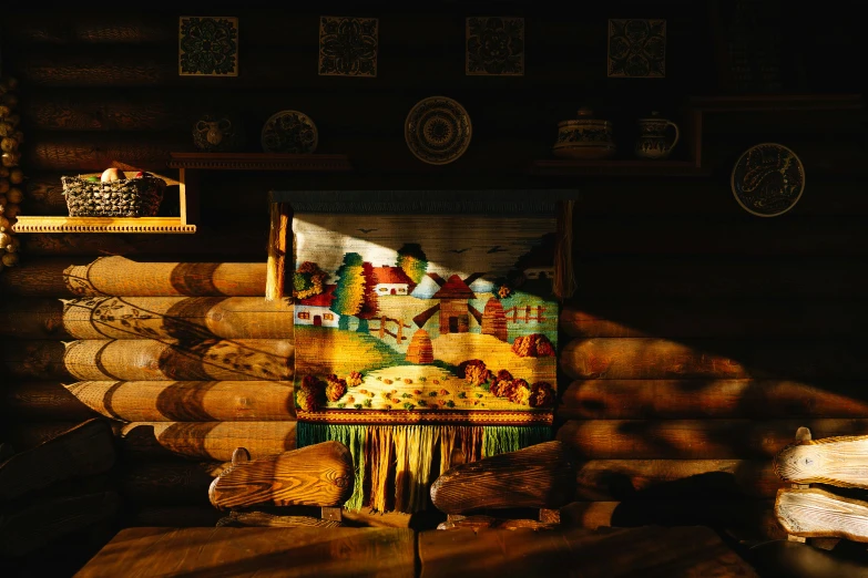 a painting sitting on top of a table in a room, inspired by Konstantin Westchilov, pexels contest winner, arts and crafts movement, inside primitive hut, golden hour photo, fabric embroidery, decorated polished wood