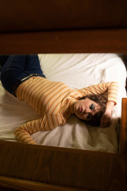 a woman laying on top of a bed in a room, a portrait, inspired by Nan Goldin, pexels, serial art, still from stranger things, striped, cinematic outfit photo, looking down