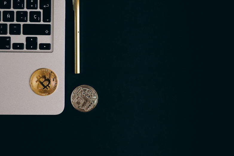 a laptop computer sitting on top of a desk next to a coin, by Julia Pishtar, trending on unsplash, edible crypto, gold and black blu, plain background, one contrasting small feature