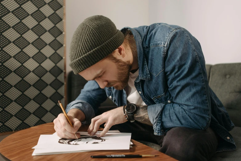 a man sitting on a couch writing on a piece of paper, a drawing, trending on pexels, academic art, artist wearing overalls, caracter with brown hat, tattoo sketches, physical painting