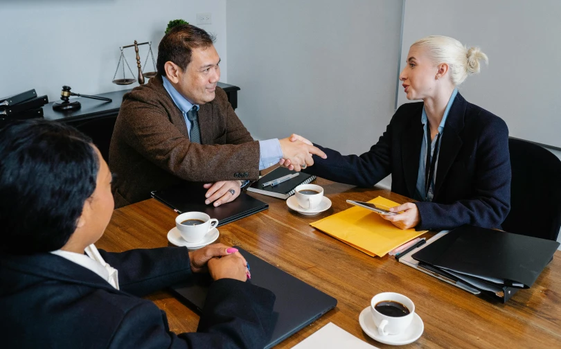 a group of people sitting around a wooden table, lawyer suit, shaking hands, cindy avelino, thumbnail