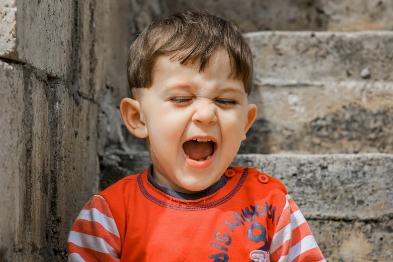 a little boy that is sitting down with his mouth open, pexels contest winner, sneering roman legioneer, tinnitus, coloured photo, clenching teeth