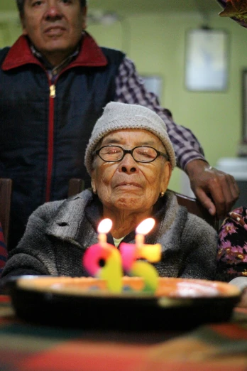 a woman sitting in front of a cake with lit candles, he is about 8 0 years old, associated press photography, chilean, person in foreground