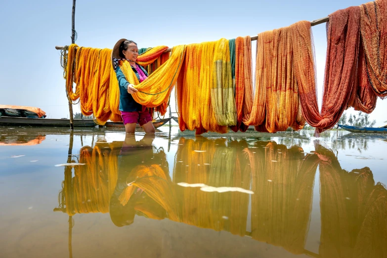 a woman standing next to a body of water, inspired by Steve McCurry, colourful clothes, laundry hanging, with yellow cloths, assamese